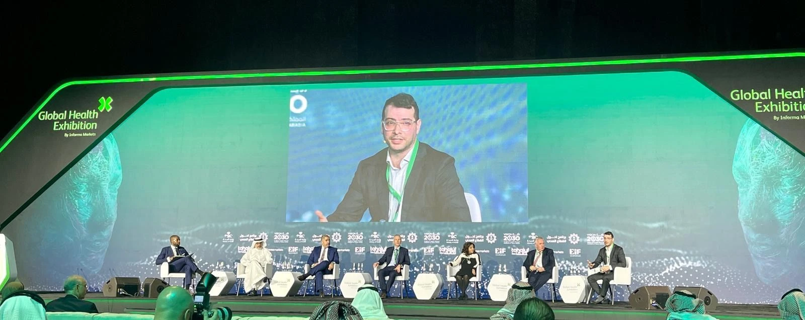 Marc Succi on stage and on the screen during a Global Health Exhibition panel in Riyadh.